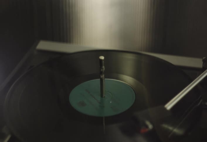 A closeup of a record player with a vinyl record spinning on the turntable the arm of the record player with the needle is visible on the right side of the frame poised above the grooves of the record
