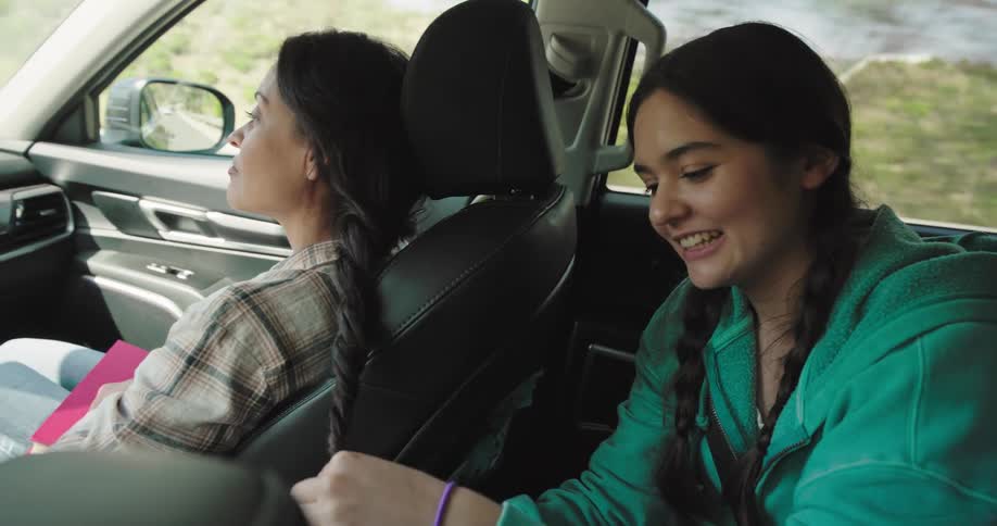 Daughter braiding moms hair from the back seat while on a road trip