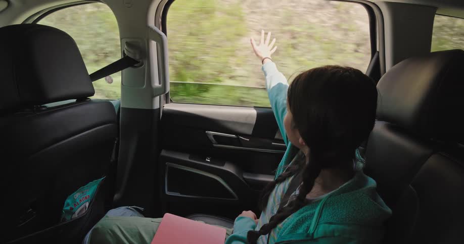 Girl extending her arm out of the window of a moving car