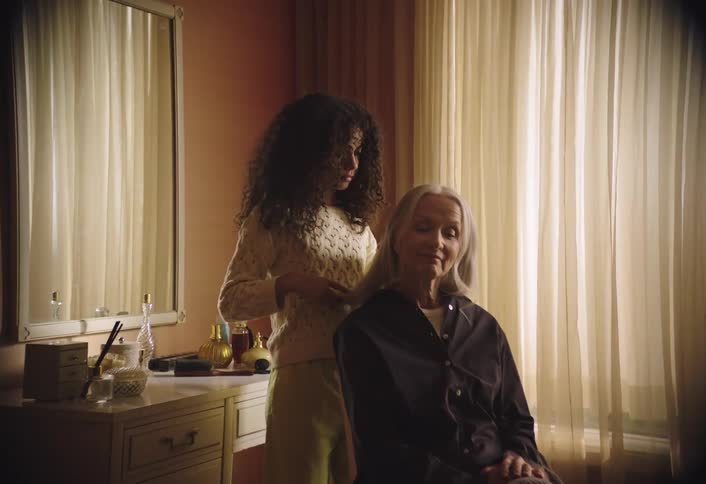 Curly haired child combing hair of lady sitting on chair