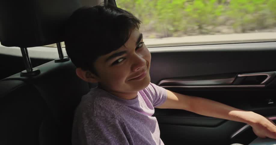 A boy is seen resting in the back seat of a car with the scenic view of a mountainside visible outside the window the camera then pans to reveal a man driving and he glances briefly at the boy through the rearview mirror