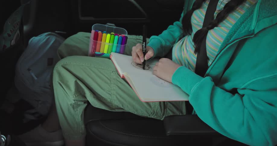 Girl drawing while sitting in the backseat of a moving car