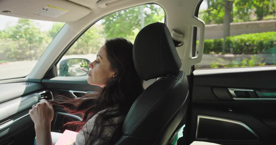 A woman sits in the passenger seat of a car looking out the window while playing with her hair