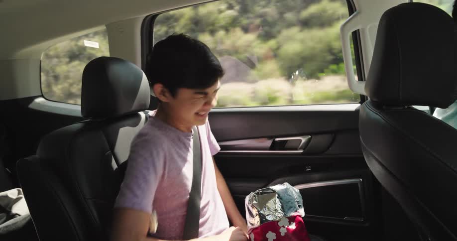 A boy laughs and throws popcorn in the car
