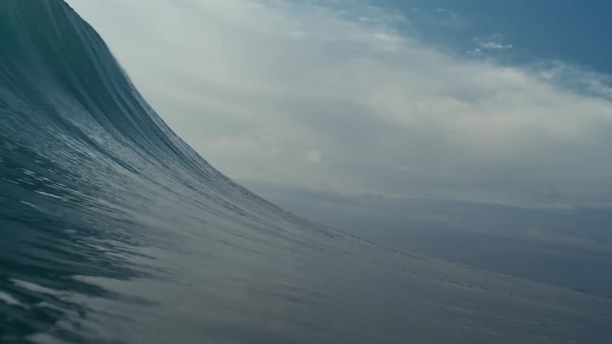 A huge wave forms and crashes across the ocean surface during daytime