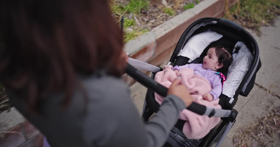 Mother pushes her daughter in a stroller while walking along a sidewalk
