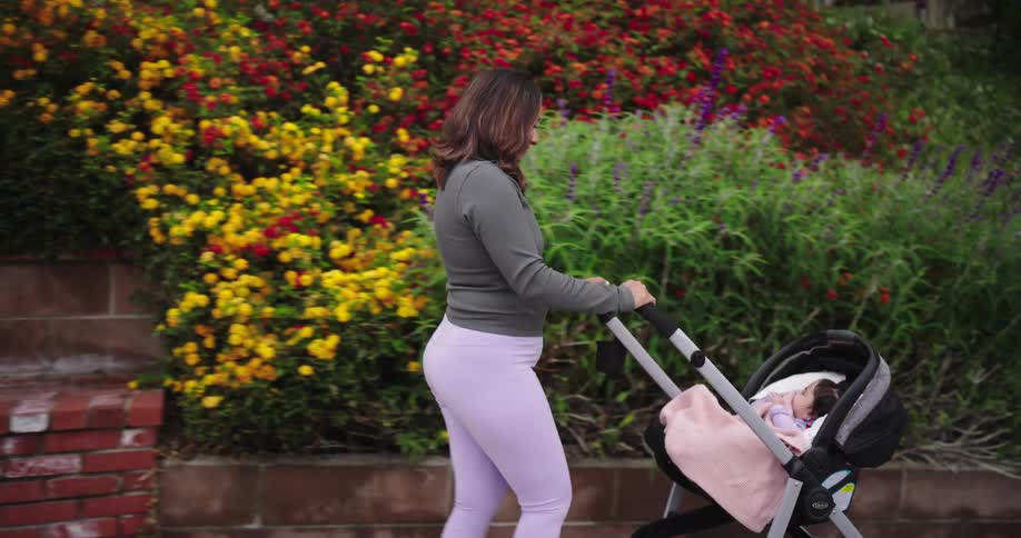 Mother pushing a baby carriage past a flower garden and a staircase pauses to adjust a baby blanket