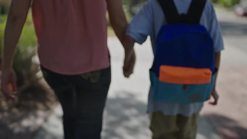 Back view of mother walking hand in hand with son carrying backpack
