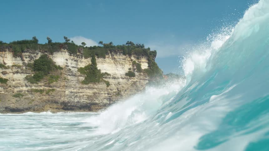 The large wave crashes on the steep shore line