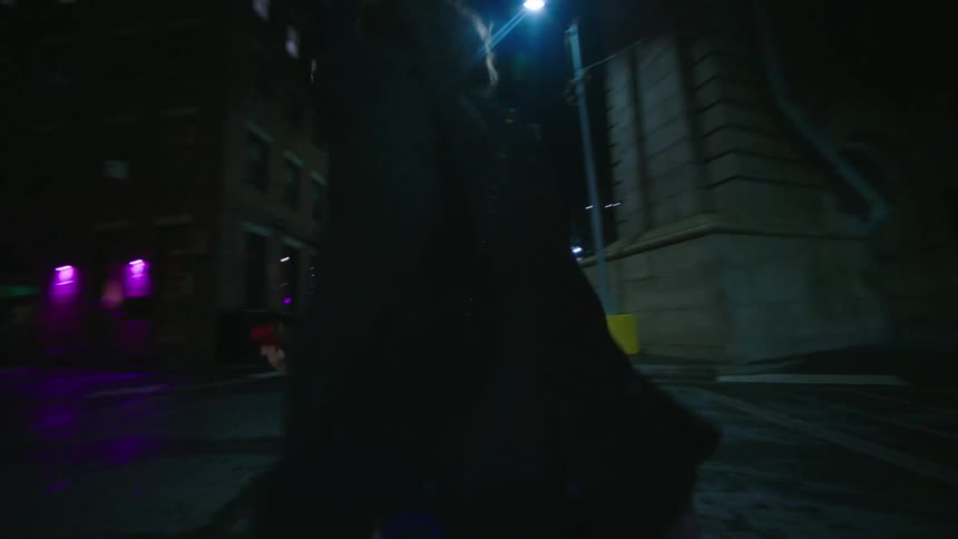 A couple walks down a cobblestone street at night with the glow of city lights reflecting on the wet pavement