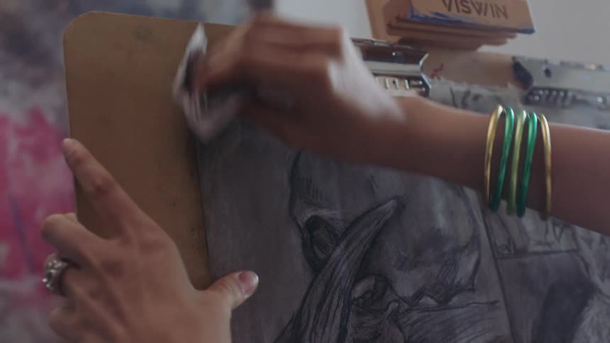 A closeup of hands erasing charcoal on a sketchpad in an art studio