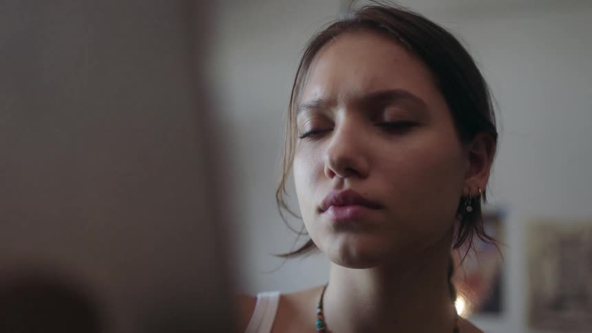 The video focuses on a woman in a white tank top and a necklace looking offcamera with a thoughtful expression her gaze appears fixed and serious only occasionally softening into a slight smile