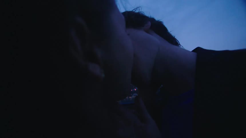 A young couple is romantically hugging and kissing on a rooftop in the evening with the cityscape in the background