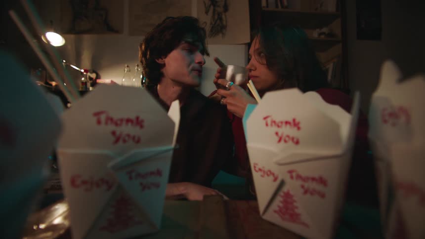A young couple is drinking from wine glasses after eating chinese takeout indoors enjoying the moment