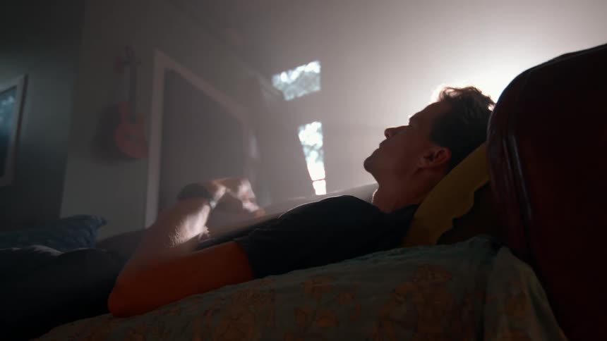 A man stops reading to rest on the couch