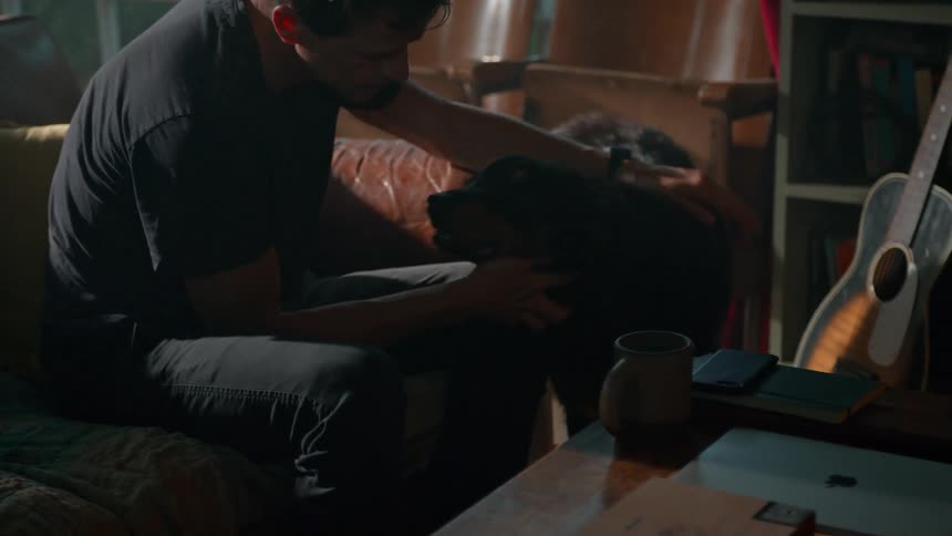 A man pets his dog while sitting on the couch
