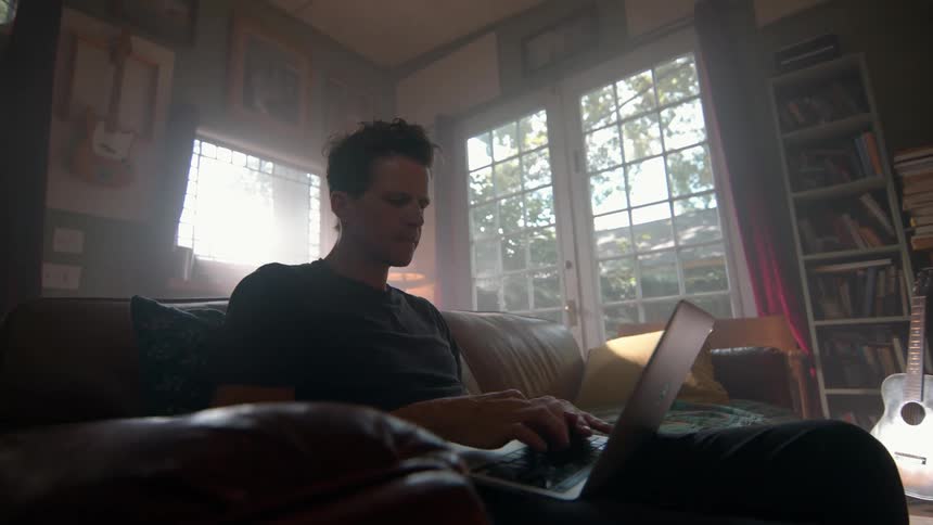 Man sitting on a sofa typing on a laptop