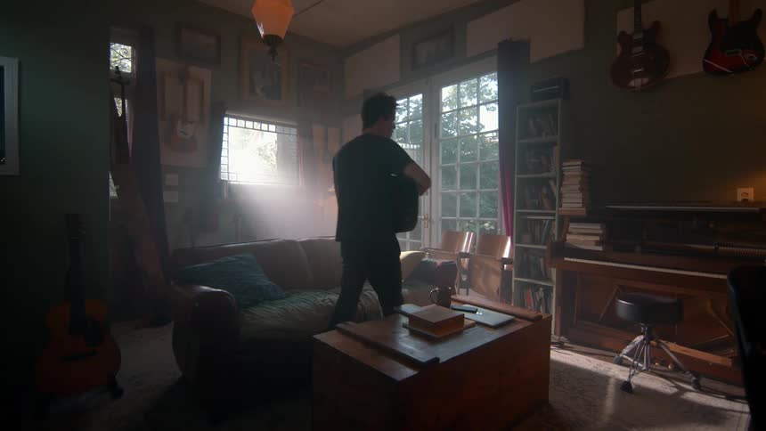 A young man playing an acoustic guitar while walking around a living room