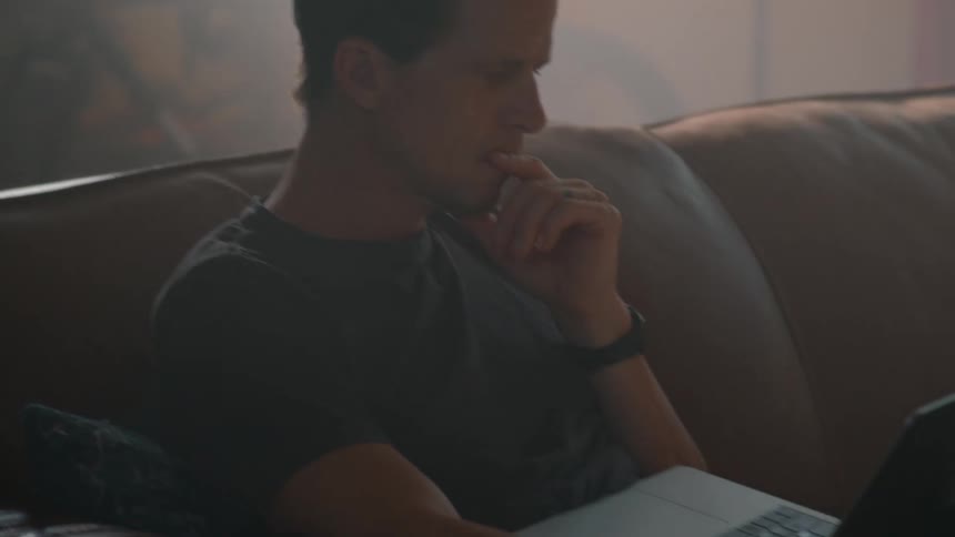 Thoughtful man sitting on a sofa with an open laptop on his lap