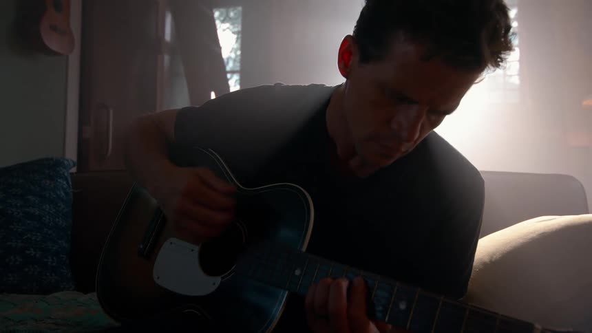 The man is playing the guitar on the couch