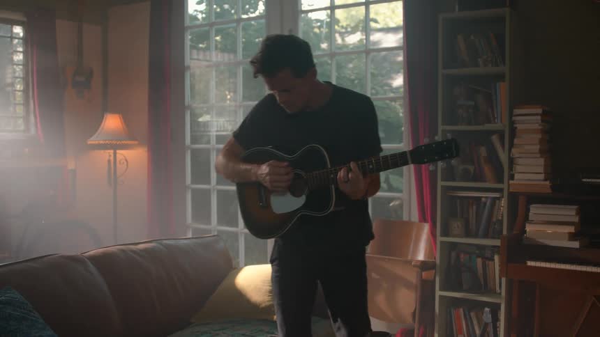 Young man plays a guitar while walking in a living room during daytime
