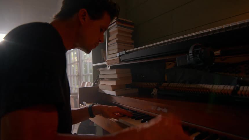 A man sits on a stool playing the piano