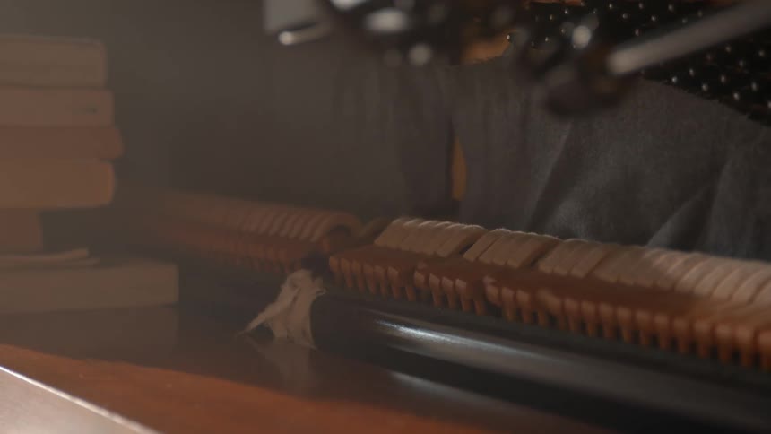 A closeup of a pianos internal mechanism shows the hammers and strings with a stack of books positioned in the background