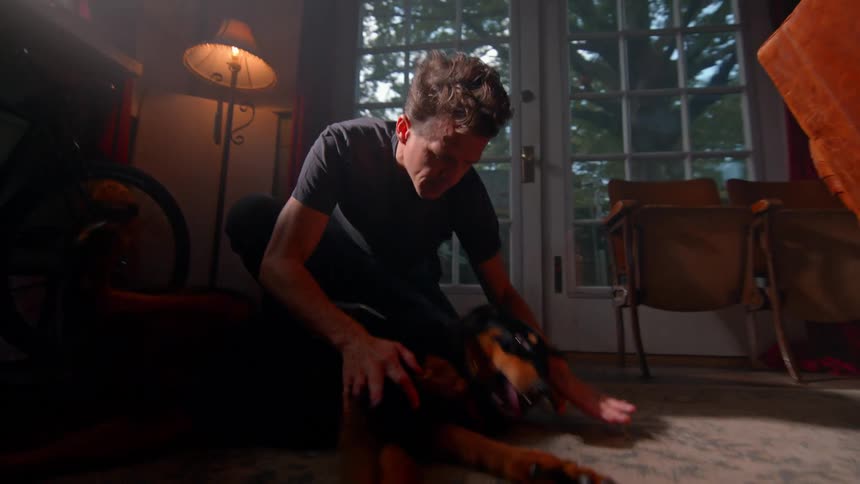 A man rubs and hugs his dog on the floor
