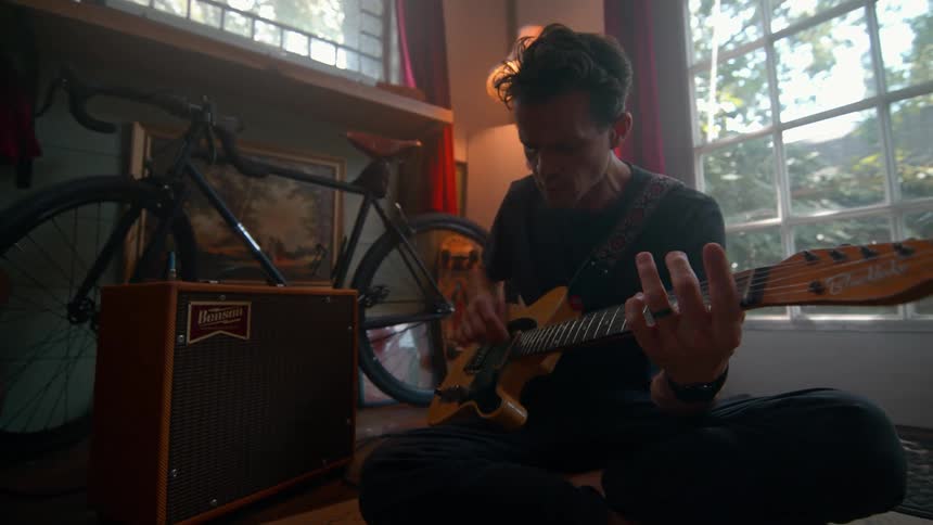 A young man sitting on the ground playing a guitar next to a bicycle
