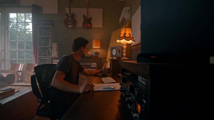 A man works at a music production desk surrounded by instruments and warm vintage decor