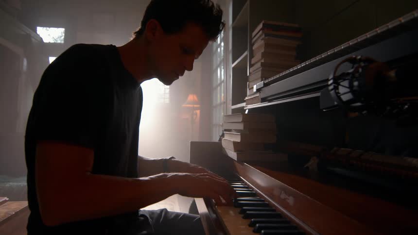 A young man approaches a piano and sits on the bench in front of it and then begins to play it