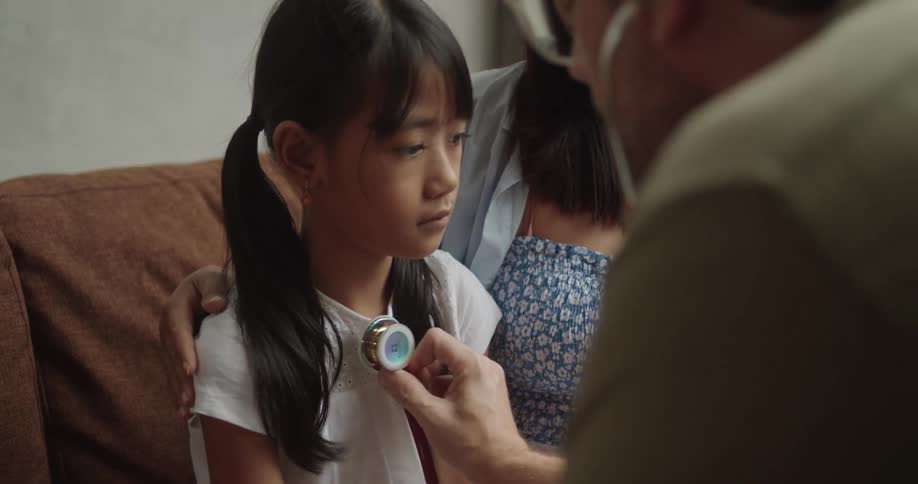 A young girl sits calmly while a healthcare professional listens to her chest with a stethoscope
