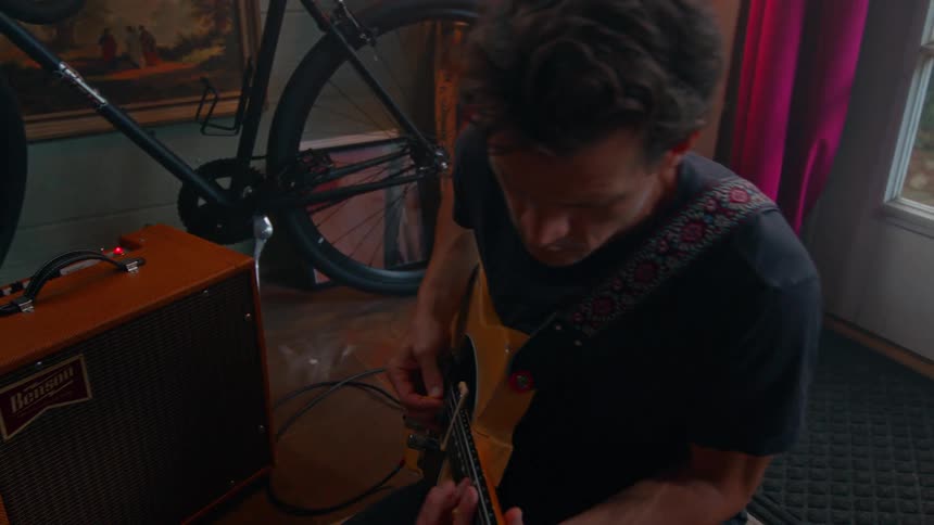 A man sits on the floor and strums his guitar