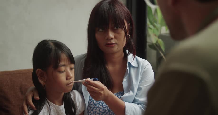 A mother puts a thermometer in her daughters mouth
