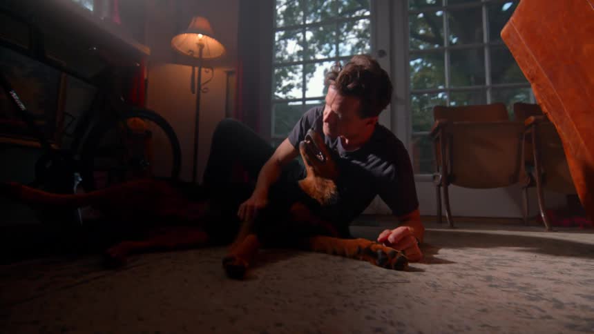 Man sitting on living room rug playing with dog