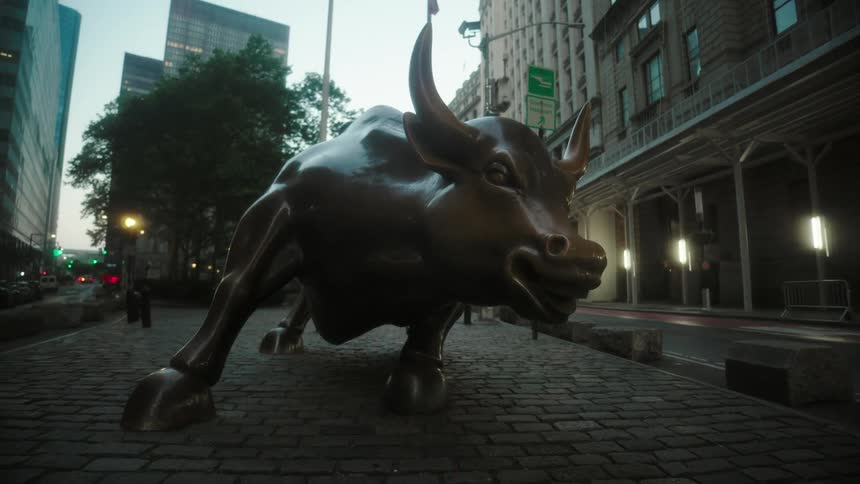 The wall street bull statue stands on cobblestones on a manhattan street at dawn