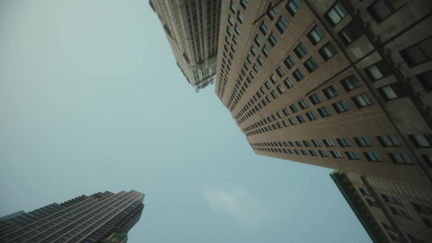 A low angle view looks up at four tall city buildings with various window patterns all converging towards a pale blue sky