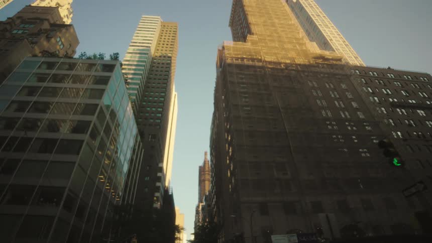 Sunlight glows on towering city buildings along a narrow street