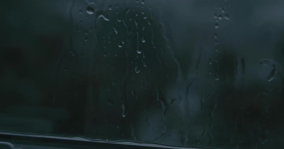 A foggy window streaked with rainwater partially reveals a blurred overcast scene outside