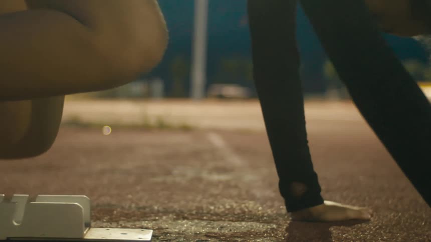 A runners feet and hands are braced in starting blocks on a track positioned for a sprint