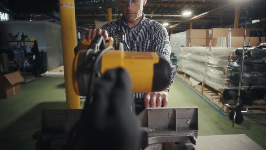 A person operates a yellow power tool in a cluttered warehouse filled with stacked materials and equipment