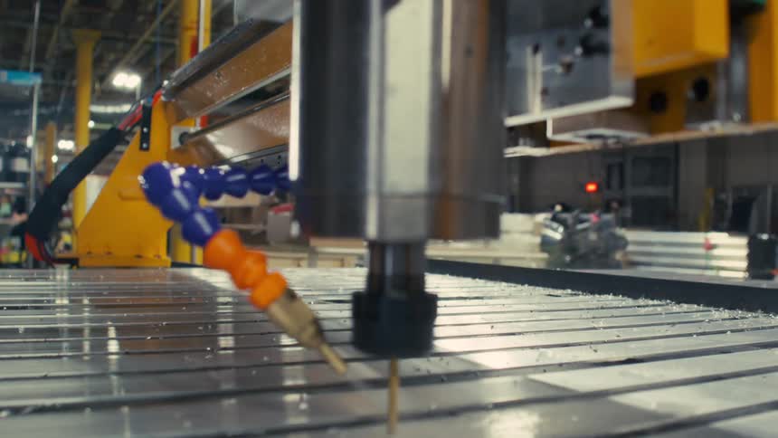 A cnc machine actively drills into a metal workpiece with industrial equipment and control panels visible in the surrounding workspace