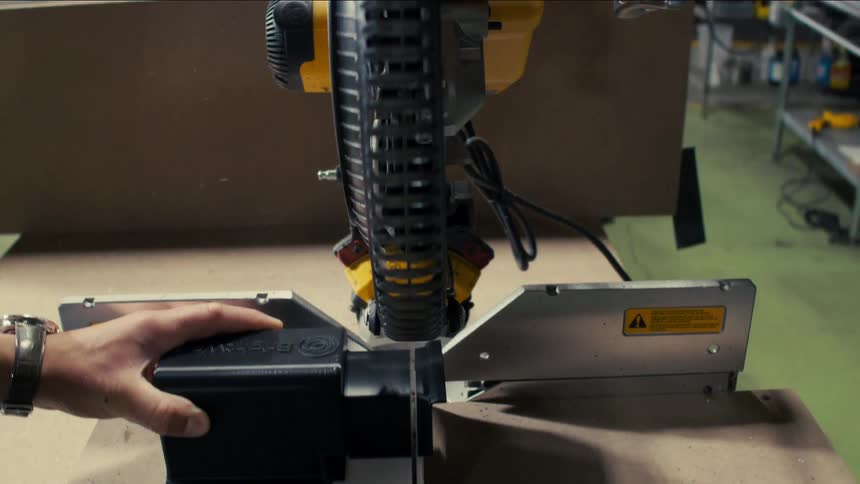 A person uses a miter saw to cut wood in a workshop surrounded by tools and shelves
