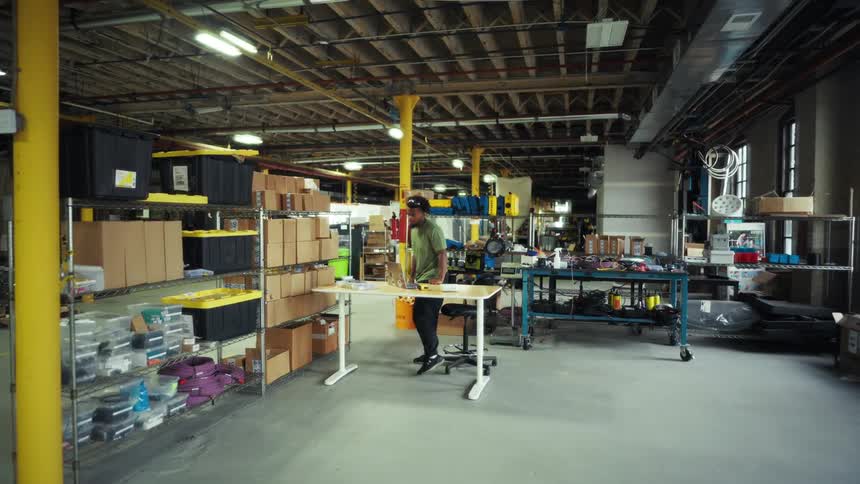 Man sitting at a factory desk getting up and picking up a box