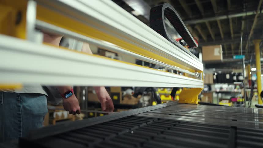 A worker operates a large industrial machine in a warehouse filled with equipment and boxes