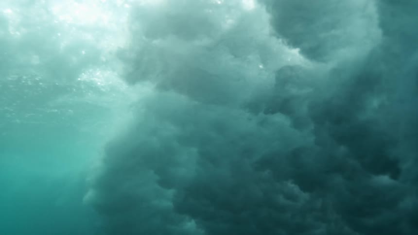 A dramatic underwater view captures the curvature and motion of a large ocean wave