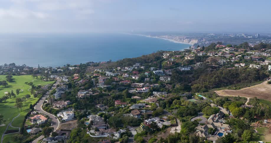 A scenic coastal neighborhood sprawls across lush hills overlooking a long stretch of beach