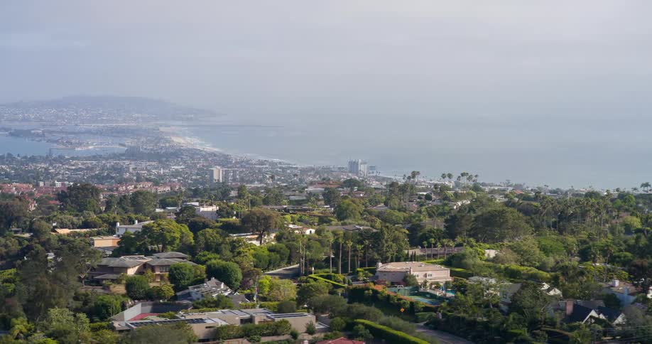 A coastal city stretches along the shoreline with dense tree cover midrise buildings and a distant view of ocean waters