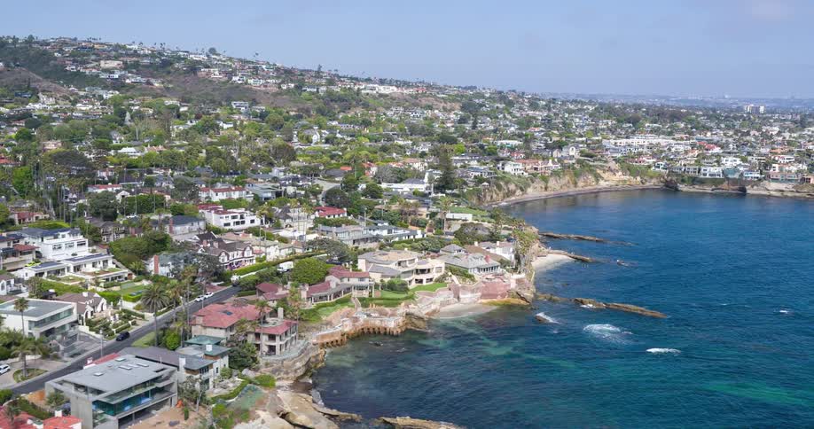 A scenic coastline is lined with luxury homes and rocky cliffs with hills rising in the background