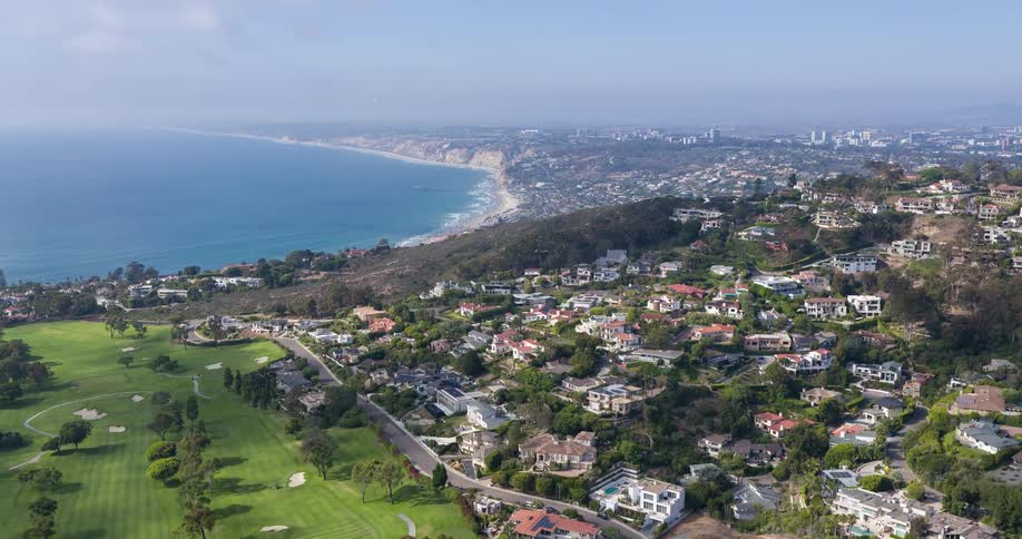 A wide suburban landscape stretches toward the ocean with homes scattered across green hills and valleys